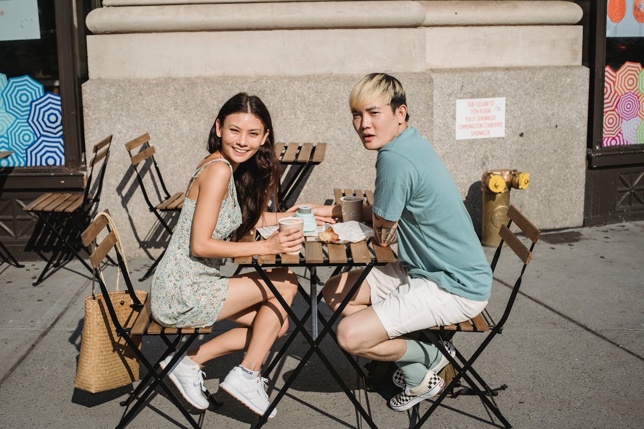 A young couple sits outdoors, sharing coffee and snacks, enjoying a sunny day.