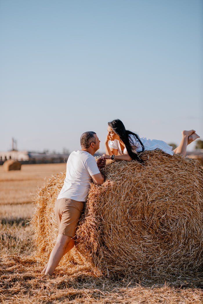 Couple enjoying a romantic moment atop a haystack in a sunny wheat field.